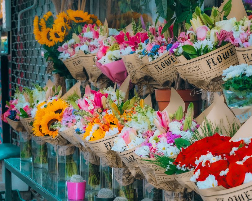 A display of fresh flower bouquets arranged on a glass shelf at the floristbeddington.co.uk shop, featuring a variety of vibrant blooms including bright yellow sunflowers, pink lilies, white and pink 